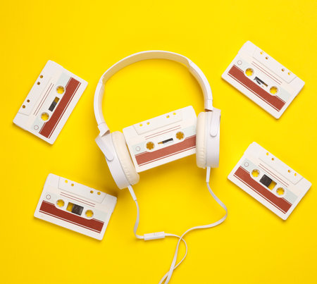 Retro 80s audio cassette with stereo headphones on yellow background. Top view. Flat layの写真素材