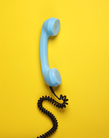Retro blue telephone receiver on yellow backgroundの写真素材