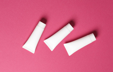 Three white cream tubes on pink background. Mockup, template for designの写真素材