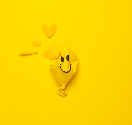Yellow Burst balloon with smiling face and hearts inside on yellow background. Love concept. Creative layoutの写真素材