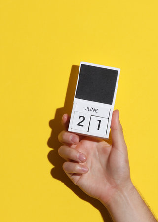 Man's hand holding wooden block calendar with date June 21 on yellow backgroundの写真素材
