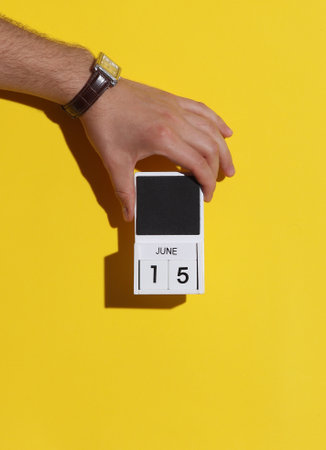 Man's hand holding wooden block calendar with date June 15 on yellow backgroundの写真素材