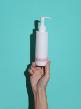 Woman's hand holds bottle of cream with dispenser on a blue background with a shadowの写真素材