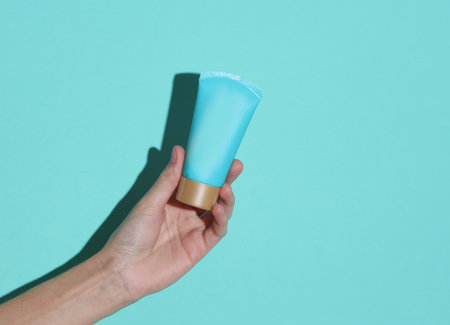 Woman's hand holds a blue tube of cream on a blue backgroundの写真素材