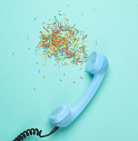 Retro telephone receiver with sprinkles on blue background. Creative layout, minimalism. Conceptual photoの写真素材