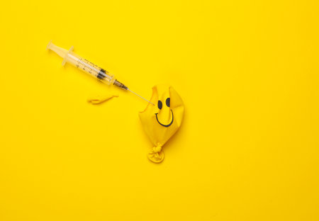 Yellow Burst balloon with smiling face and syringe on yellow background. Treatment of mental problemsの写真素材
