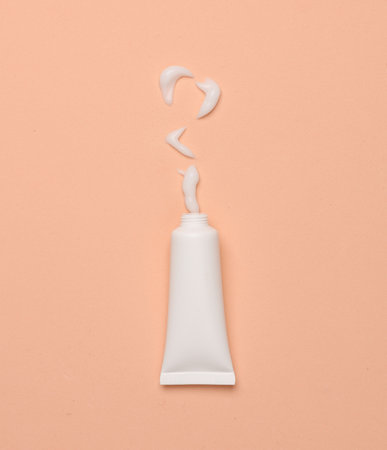 Mockup of white tube with smear of cream on pink background