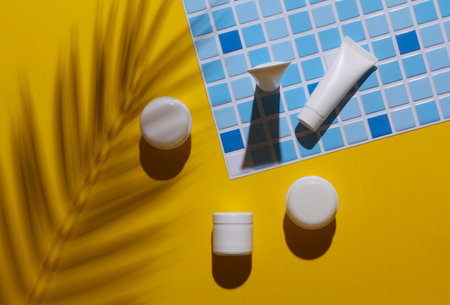 White cream tubes and jars on tile with palm leaf shadow. Creative layout. Template for design....