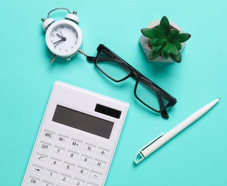 Calculator, alarm clock, pen, eyeglasses and plant on blue background. Business concept. Workspace. Top view. Flat layの写真素材