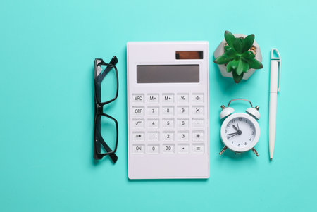 Calculator, alarm clock, pen, eyeglasses and plant on blue background. Business concept. Workspace....