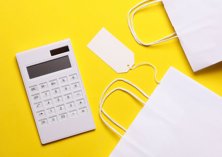 White Calculator with shopping bags and price tag on yellow background. Sale conceptの写真素材