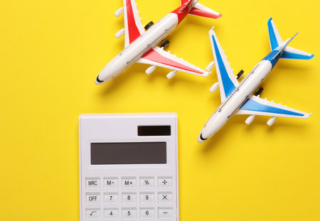 Calculator and toy aircraft model on a yellow background. Vacation cost conceptの写真素材