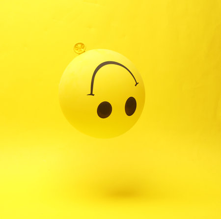 Levitation down balloon with a smile face on a yellow backgroundの写真素材