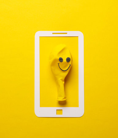 Paper-cut smartphone icon with smile face balloon on a yellow backgroundの写真素材