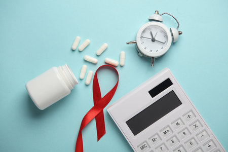 Red AIDS Awareness Ribbon, pills, alarm clock and calculator on Blue Background. Top view