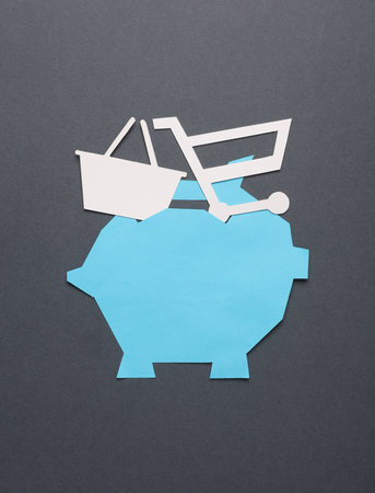 Paper-cut piggy bank with shopping basket and cart on a dark gray background.の写真素材