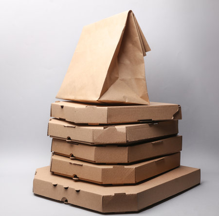 A stack of pizza cardboard boxes with a craft package on a gray background. Delivery, takeaway foodの写真素材