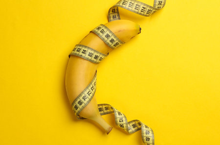 Banana wrapped with measuring tape on yellow backgroundの写真素材