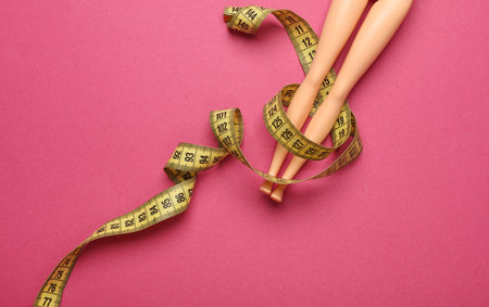 Doll legs with measuring tape on pink background. Weight loss, diet concept