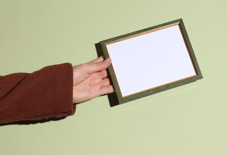 Man's hand in a coat holds an empty frame on a green backgroundの写真素材