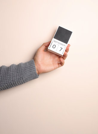 Man's hand in a sweater holds block calendar with the date September 7 on a beige background