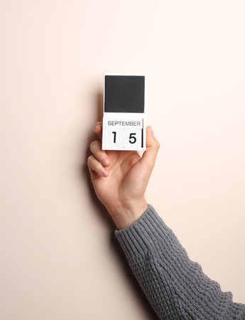Man's hand in sweater holds block calendar with the date September 15 on a beige backgroundの写真素材