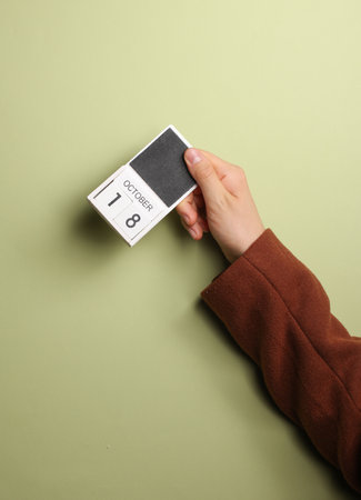 Man's hand in coat holds block calendar with the date October 18 on green backgroundの写真素材