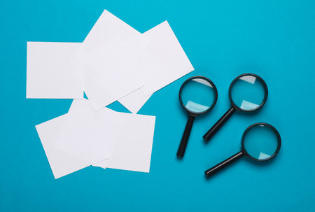 White square memo papers with a magnifying glasses on a blue backgroundの写真素材