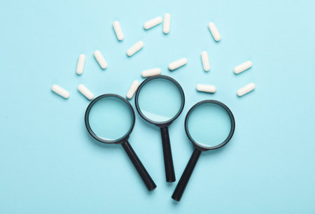 Magnifying glasses and pills on blue backgroundの写真素材