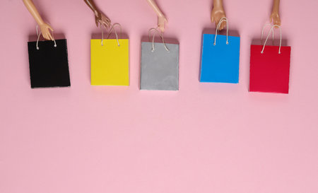 Doll hands holding Miniature shopping bags on pink background. Black Friday, world shopping day,...