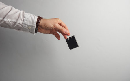 Man's hand in white shirt holds miniature shopping bag on gray background. Black Friday, world shopping day, sale conceptの写真素材