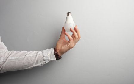 Man's hand in white shirt holds light bulb on gray background