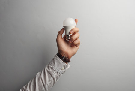 Man's hand in white shirt holds light bulb on gray background