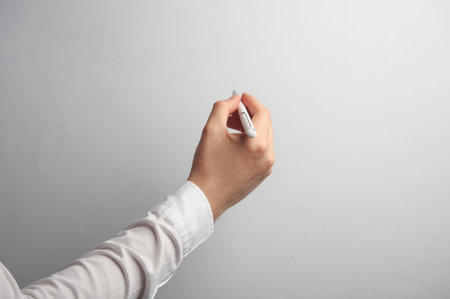 Man's hand in white shirt holds pen on gray background. Mockup for design. Business conceptの写真素材