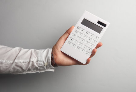 Man's hand in white shirt holds calculator on gray background. Business concapt