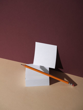 Square memo papers and pencil on beige burgundy background with shadow. Creative layout