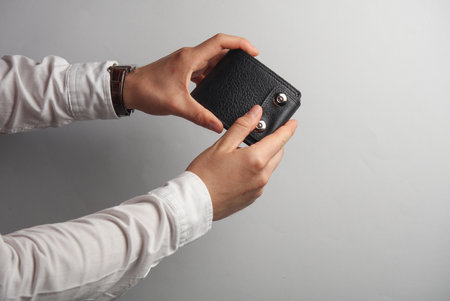 Male hands in white shirt holds leather purse on gray background