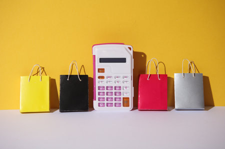 Miniature paper shopping bags and calculator on yellow gray background.の写真素材