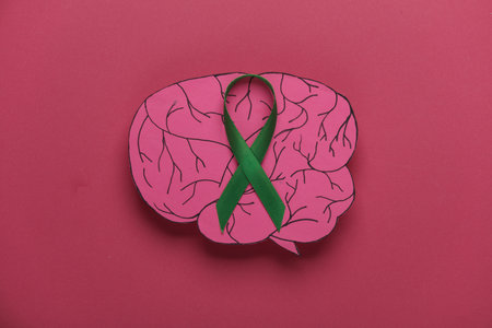 Green awareness ribbon with paper brain on a pink background. World mental health day conceptの写真素材