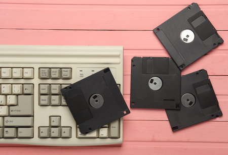 Retro floppy disks and old-fashioned keyboard on pink wooden boards. 80s technology. Top viewの写真素材