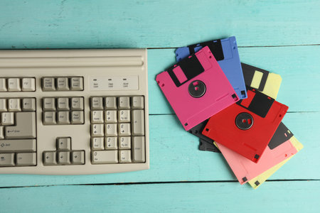 Retro floppy disks and old-fashioned keyboard on pink wooden boards. 80s technology. Top view