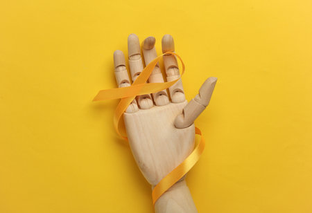 Yellow ribbon in wooden hand, childhood cancer awareness day symbolの写真素材