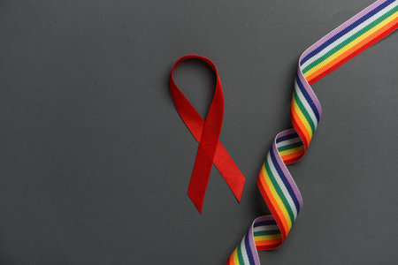 Red awareness ribbon with lgbt rainbow ribbon on dark background. Worlds HIV Aids Day