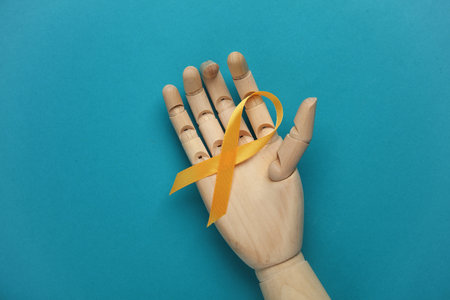 Yellow ribbon in wooden hand, childhood cancer awareness day symbol on blue backgroundの写真素材