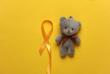 Yellow ribbon, childhood cancer awareness day symbol with teddy bear on yellow backgroundの写真素材