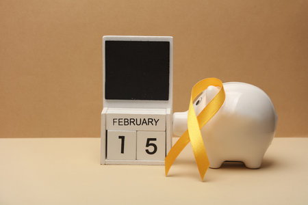 Yellow ribbon, calendar with date February 15 and piggy bank. World childhood cancer awareness day