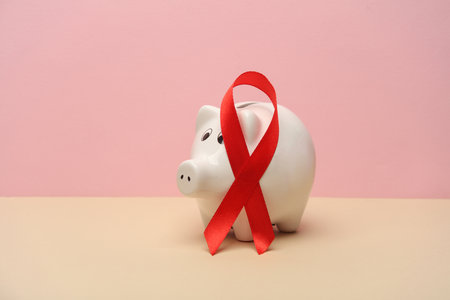 Piggy bank with Red awareness ribbon on pink background. Worlds HIV Aids Day