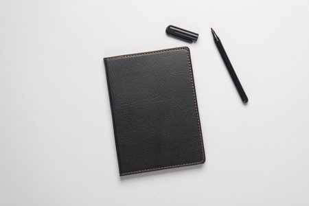 Notebook with black leather cover and pen on gray background
