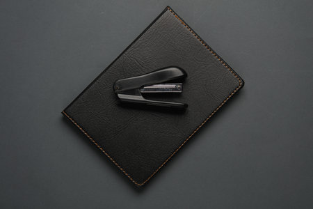 Notebook with black leather cover and stapler on dark gray background. Business concept. Top view. Flat layの写真素材