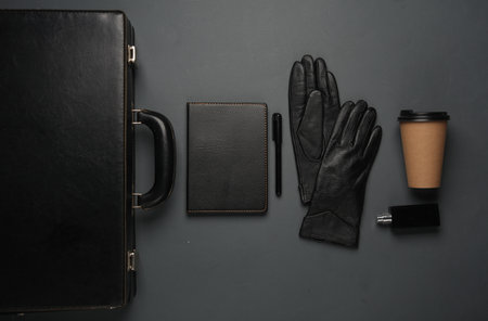 Leather suitcase with gloves, notebook, coffee cup and perfume bottle on a dark background. Business concept. Top viewの写真素材
